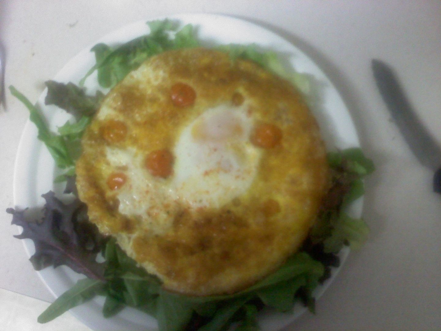 4 egg shredded chicken frittata with tiny sweet tomatoes embedded in it with another egg cooked whole on top, served atop a bed of fresh CSA salad greens